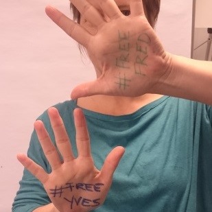 Image of a woman with for #FreeFred and #FreeYves written on the palms of her hands