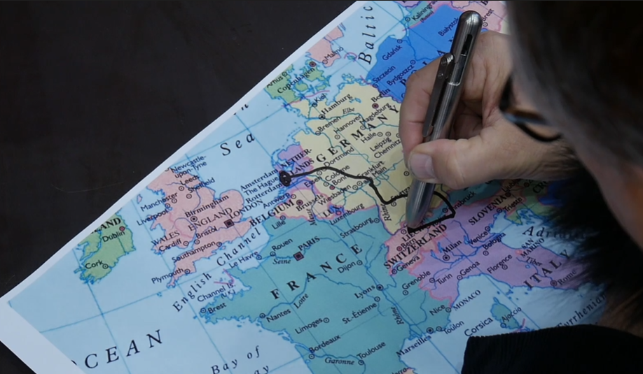 A hand drawing a route over a map of Europe